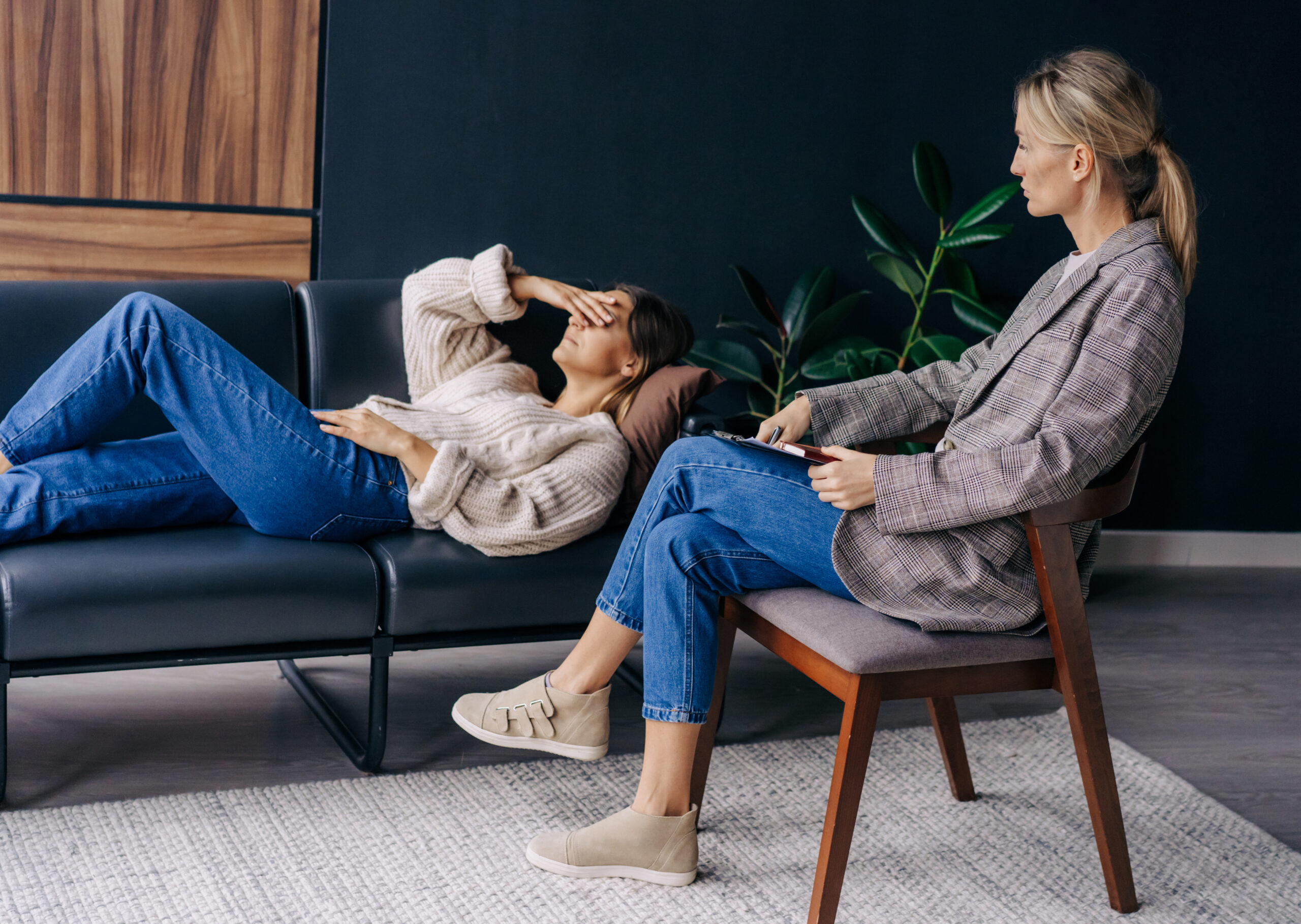 A psychoanalyst in a workshop listens to a female patient lying on a couch and talking about her problems.